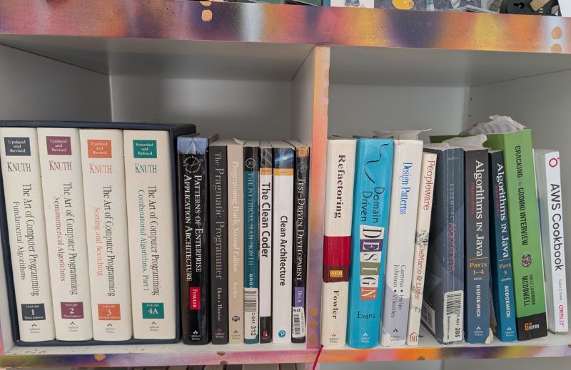 A bookshelf with foundational software engineering books, including The Mythical Man-Month, Code Complete, and Designing Data-Intensive Applications